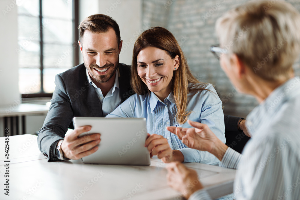 Wall mural Happy couple using digital tablet while having a meeting with their insurance agent in the office