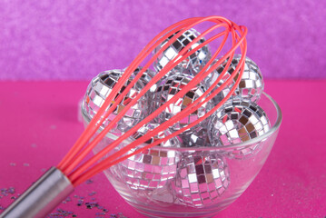 Magic party concept. Small toy discoballs in glass plate and kitchen whisk on purple, pink background. Small silver stars around. Soft focus
