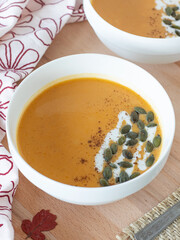 Butternut squash soup in a bowl with pumpkin seeds and coconut milk on a wooden table. Vertical shot. A close-up. Plant-based autumn meal.