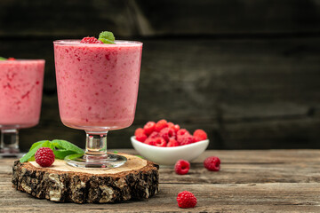 Yogurt smoothie with raspberries in glass on wooden table.