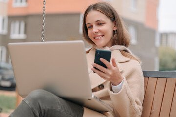 Closeup of business woman typing on laptop keyboard. Attractive woman in casual wear smiling while talking on smartphone.