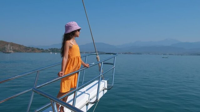 Girl on yacht deck by shore. A view of little girl on yacht deck in the clear sea water. A concept of summer relaxation in the sea.