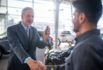 Car dealer giving an handshake and giving keys to seal the deal for new car