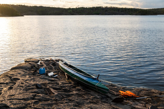 Blue kayak on the rocky shore of a large lake. Nearby are things of a traveling tourist