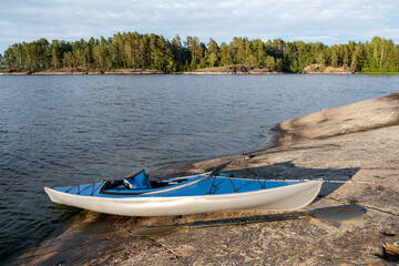 Blue kayak on the stone of a large lake. An oar lies on a rocky shore. Spinning for catching fish on the bow of the boat