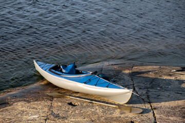 Blue kayak on the stone of a large lake. An oar lies on a rocky shore. Spinning for catching fish on the bow of the boat