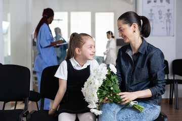 Smiling little girl chatting with mother in medical clinic waiting room. Happy family members waiting to see hospitalized relative at sanatorium. Visiting room of busy hospital.