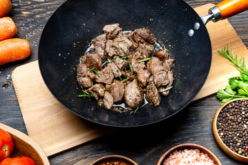 Beef fillet fried with vegetables in a wok. Argus in the wok. Top view of the kitchen table with spices and vegetables.