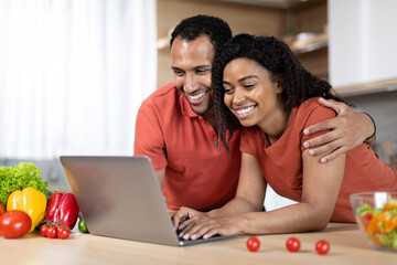 Glad young black guy in red t-shirt hugging his wife, have video call on computer at table
