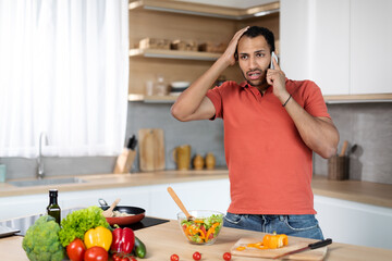 Sad confused young african american guy in red t-shirt holds his head with hand calls by phone, got...