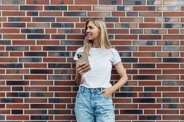 woman in a white t-shirt with copy space holding a mobile phone and looking to the side against a background of wall