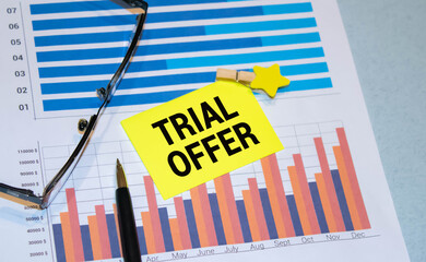 a white card with the text trial offer on the background of an open paper notebook and a metal pen.