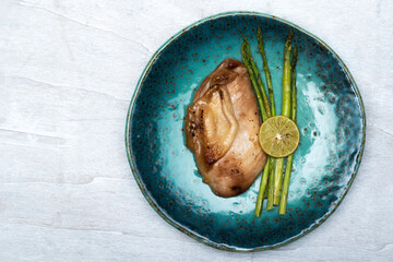 Healthy food chicken grill with lemon and asparagus in blue plate on white wood background top view.