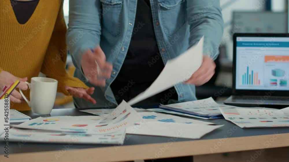 Poster selective focus on coworkers hands going through business papers with sales charts and key profit in