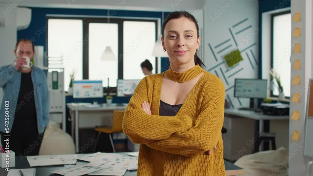 Poster portrait of confident startup employee entering frame posing with arms crossed and smiling in busy m
