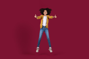Happy black girl jumping up, showing thumb ups, isolated