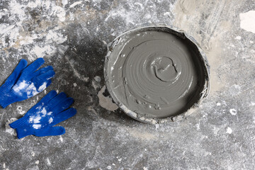 Bucket of concrete and gloves on floor indoors, flat lay