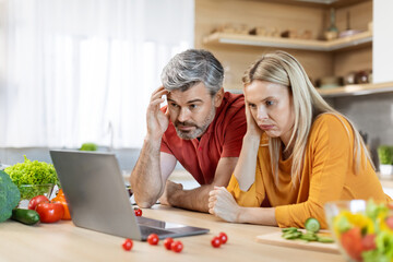 Confused middle aged spouses cooking together, reading food blog