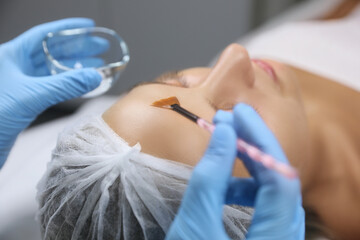 Cosmetologist applying chemical peel product on client's face in salon