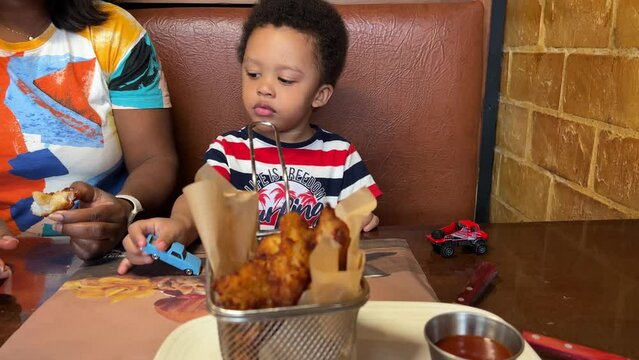 Cute And Expressive  Two-year-old Mixed Race Child Eating Chicken Fingers In A  Burger Restaurant Seated Next To Mum.