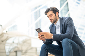 Closeup of young caucasian serious man using modern smartphone device while sitting at the public area, while looking at the social network on smartphone.