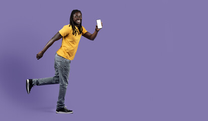 Excited african american man with smartphone running over purple