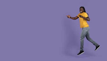 Fototapeta na wymiar Excited black guy running towards copy space on purple