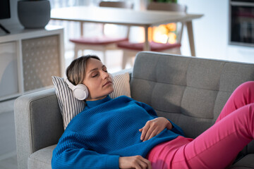 Peaceful calm young woman with closed eyes relaxing on sofa, listening to meditative music in...