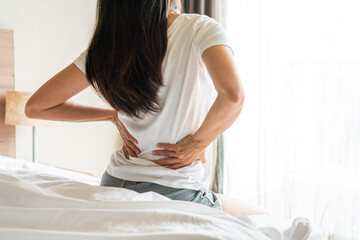 Back view of Asian woman suffering from backache sitting on bed in bedroom at home. Unhappy girl feel back pain due to mattress too soft. Health problem concept. close up, copy space