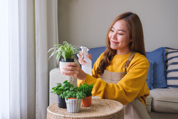 Portrait image of a beautiful young woman taking care and watering houseplants with plant mister spray at home