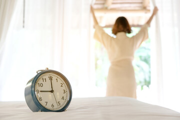 Morning of a new day, alarm clock wake up woman sitting in the room. A woman stretch the muscles at window. Health and care concepts