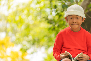 Cute boy in red shirt is happily reading book.