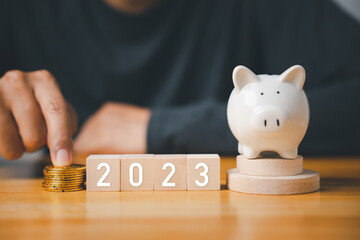 Happy New Year 2023. Businessman with wood cubes block number years 2023 and piggy bank to setting...