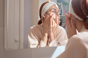Beauty Day. Woman doing her daily skincare routine in bathroom and mirror gently puts cream on her...