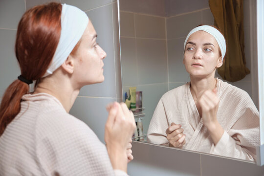 Beauty Day. Woman doing her daily skincare routine in bathroom and mirror gently puts cream on her face and spears it until it is absorbed. Concept of beauty, self-care, cosmetics, youth.