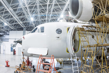 Close-up white transport airplane in the hangar. Aircraft under maintenance. Checking mechanical systems for flight operations