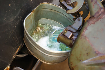 a man in gloves pours fuel from a canister into the tank of a rusty car