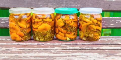 four glass jars with pickled mushrooms and saffron milk caps are on the bench