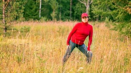 Naklejka na ściany i meble beautiful mature women doing gymnastics in a clearing in a coniferous forest on a summer day