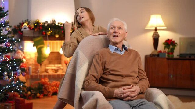 Joyful grandfather singing Christmas carol with teen granddaughter in living room at home. Portrait of carefree relaxed Caucasian senior man and teenage girl enjoying New Year's eve indoors