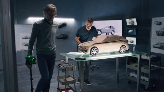 Two male automotive designers working on eco friendly model of electric car in modern car design studio. One sculpting with plasticine clay, other working in 3D modeling computer software.