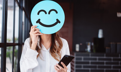 Asian woman holding blue happy smile face on paper cut, user giving good feedback rating, think...