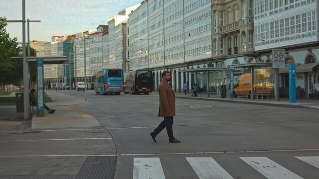 A businessman in a coat crosses the road at a pedestrian crossing in the city center in the morning.