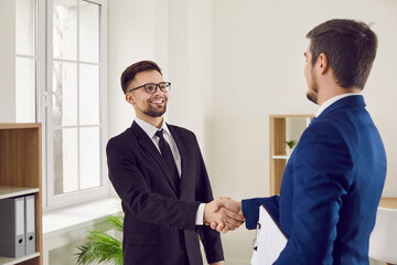 Two happy men meeting in office, making business deal and shaking hands. Happy client satisfied with good professional help exchanges handshakes with professional estate agent, loan broker or lawyer
