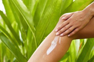 Skincare. Bodycare. Human body part. Woman applying cream or scrub on her leg against tropical green leaves background