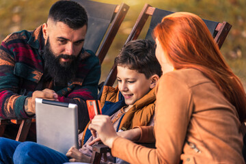 Young family enjoying time in a outdoor cafe using digital tablet for online shopping.