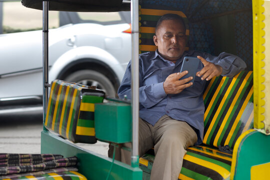 Auto driver using mobile phone while sitting inside auto rickshaw
