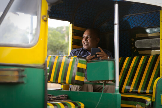Auto driver using mobile phone while sitting inside auto rickshaw