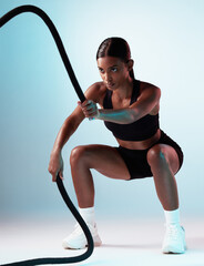Battle rope, exercise and fitness model in a studio with energy, motivation and training. Healthy, strong and slim woman athlete from India doing a cardio sports workout isolated by a blue background