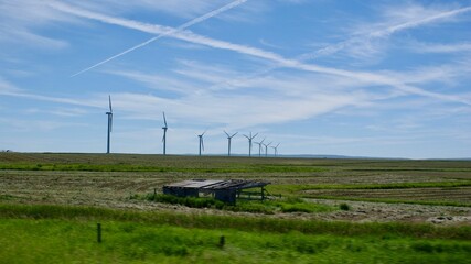 Row of wind turbines at a distance spinning in lush green field under blue cloudy sky